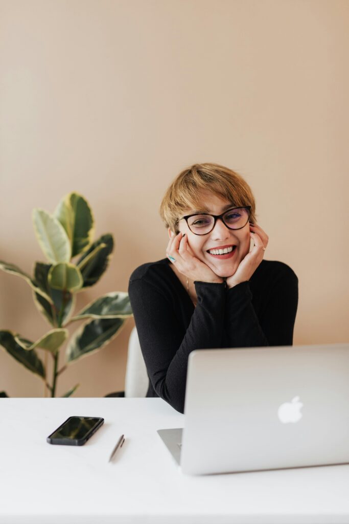 Cheerful woman smiling while sitting at table with laptop